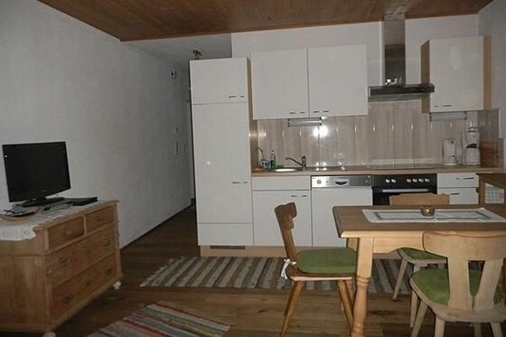 Kombinierter Wohn- und Essbereich mit weißer Küchenzeile, Holztisch und Fernseher auf einer Kommode.