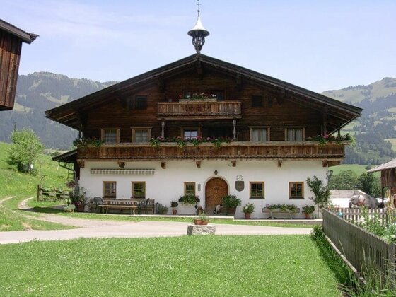 Traditionelles Alpenhaus aus Holz und weißem Putz mit Blumenbalkonen vor bewaldeten Bergen.