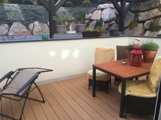 Terrasse Appartement Lyso Möblierte Terrasse mit Holztisch, Stühlen mit Fellauflagen und einer Sonnenliege vor einer Steinmauer.