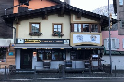 Außenansicht der Flannigans Sports Bar in Kitzbühel mit dunklen Markisen und Holzfassade.