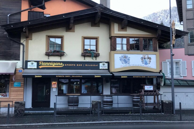 Außenansicht der Flannigans Sports Bar in Kitzbühel mit dunklen Markisen und Holzfassade.