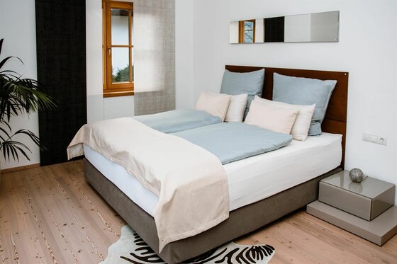 Modernes Doppelbett mit hellblauer Bettwäsche in einem hellen Zimmer mit Holzboden.