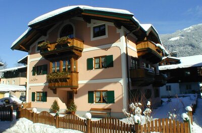 Mehrstöckiges alpines Wohnhaus mit Holzfassadenelementen und schneebedecktem Dach unter blauem Himmel.
