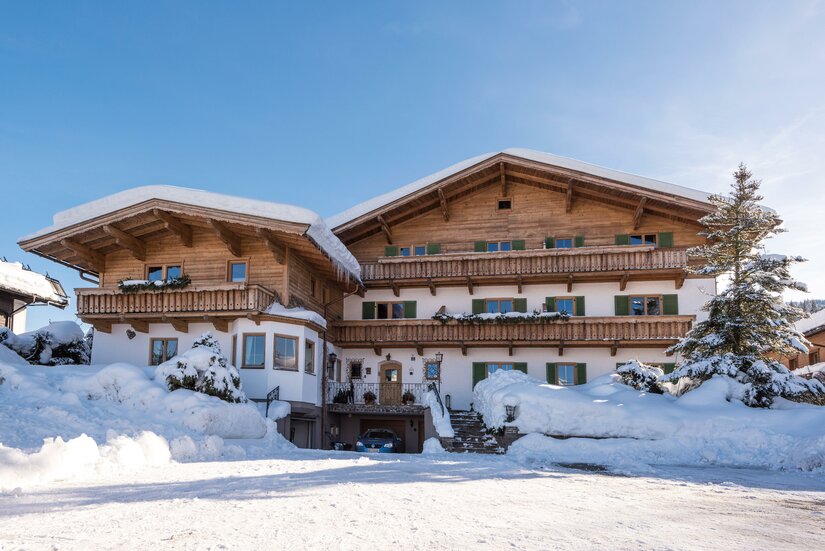 Alpines Holzhaus mit Balkonen im Schnee unter blauem Himmel.