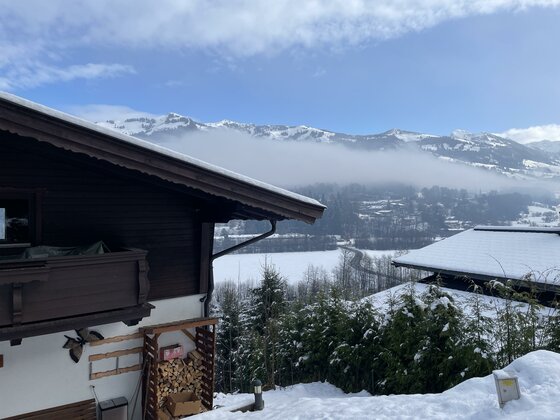Blick von einem Holzhaus auf eine verschneite Berglandschaft mit Nebelbank im Tal.