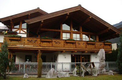 Alpines Wohnhaus aus Holz und weißem Putz mit großem Balkon und Garten.