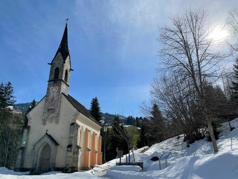 Kapelle in Kochau Kleine Kapelle mit spitzem Turm in einer verschneiten Winterlandschaft unter blauem Himmel.