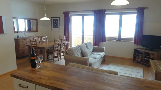 Wohnbereich Fraser Wohnungen Wohn- und Essbereich mit Holzmöbeln, hellem Sofa, Fernseher und großer Fensterfront.
