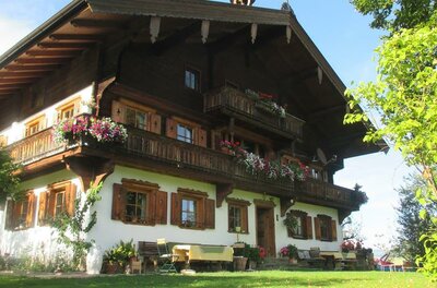 Sommer am Plattenhof Traditionelles Alpenhaus mit Blumenbalkonen und weißer Fassade unter blauem Himmel.