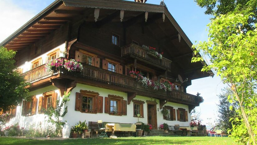 Sommer am Plattenhof Traditionelles Alpenhaus mit Blumenbalkonen und weißer Fassade unter blauem Himmel.