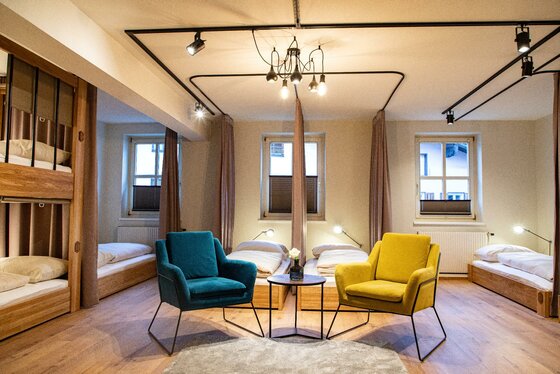 Schlafsaal im Safestay Kitzbühel Moderner Schlafsaal mit Holzbetten, zwei bunten Sesseln und einem kleinen Beistelltisch.