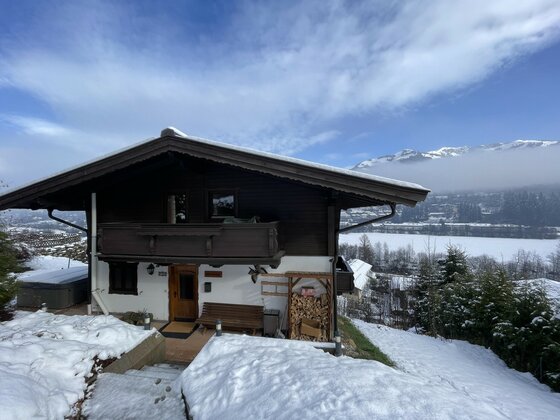 Zweistöckiges Holzchalet in verschneiter Berglandschaft mit Balkon und Brennholzstapel.
