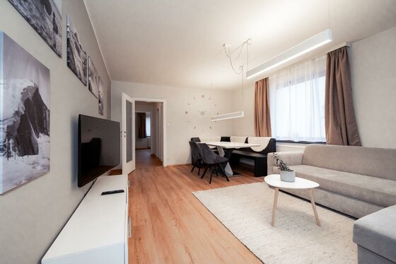 Kitzbühel_DeNi Apt_Wohnzimmer Large Ein modernes Wohnzimmer mit einem grauen Sofa und einem weißen Couchtisch. An der Wand hängen Bilder, und der Raum ist hell und freundlich gestaltet.