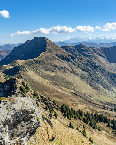 Ein atemberaubender Blick auf die Berge, wo grüne Wiesen auf schroffe Felsen treffen, während Wolken sanft am Himmel treiben.