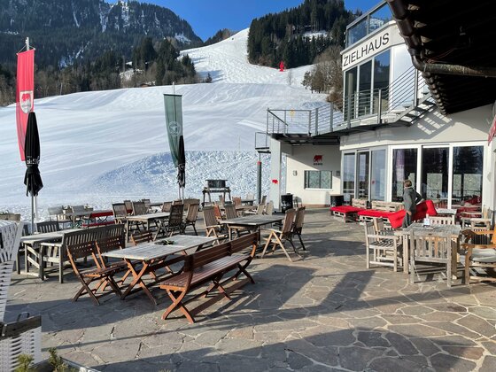 Eine gemütliche Terrasse eines Restaurants in den Bergen. Im Hintergrund sieht man Schnee und eine wunderschöne winterliche Landschaft.