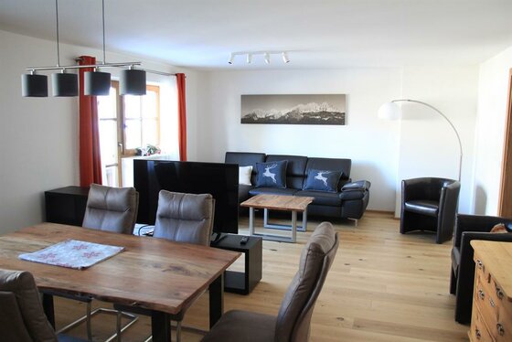 Moderner Wohn- und Essbereich mit Holztisch, dunklem Sofa, Fernseher und Parkettboden.