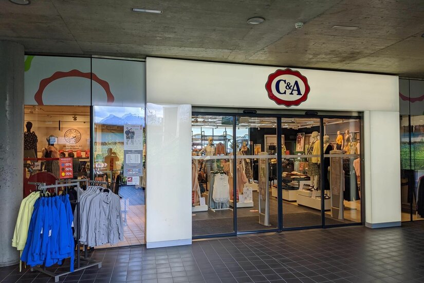 Eingangsbereich einer C&A Filiale mit Schaufenstern und Kleiderständern unter einer Betondecke.