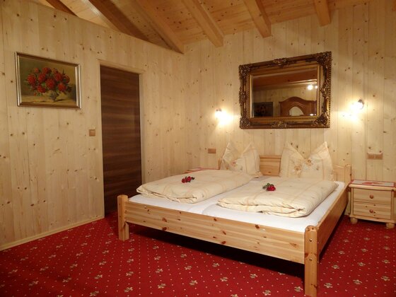 Doppelzimmer im Gasthof Möllinger Doppelbett aus hellem Holz in einem Zimmer mit Holzvertäfelung und rotem Teppichboden.