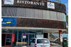 Ein Restaurant mit der Aufschrift "Ristorante" und einer Terrasse. Vor dem Gebäude steht ein weißes Auto auf einem Parkplatz.