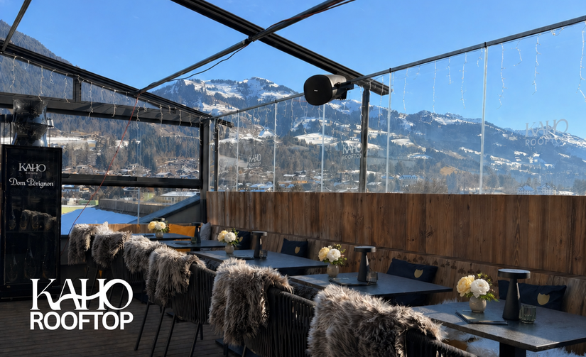 KAHO Rooftop Terrasse Moderne Dachterrasse mit Tischen, Stühlen mit Fellauflagen und Blick auf schneebedeckte Berge.