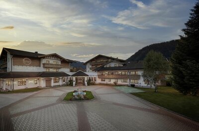 Lisi Family Hotel Sommer Außenansicht des Lisi Family Hotels mit gepflastertem Vorplatz und Springbrunnen in der Dämmerung.