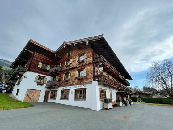 Mehrstöckiges alpines Gasthaus mit weißem Erdgeschoss und dunkler Holzfassade in den Obergeschossen.
