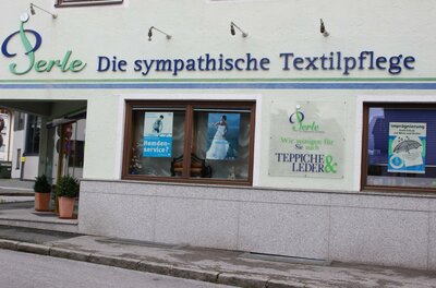 Ein Geschäft mit der Beschriftung „Perle - Die sympathische Textilpflege“. Es bietet Dienstleistungen für Textilien und Leder an.