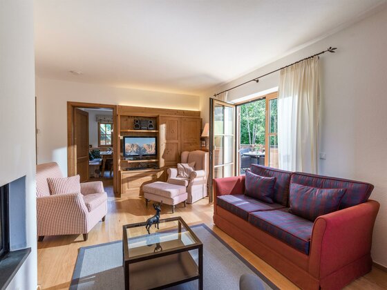 Wohnzimmer mit rotem Sofa, Sesseln, Holzeinbaumöbeln und Balkonzugang.