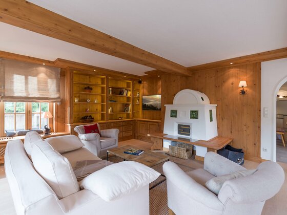 Wohnzimmer mit hellen Sofas, Holzverkleidung an Wänden und Decke sowie einem weißen Kachelofen.