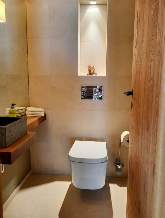 Modernes Badezimmer mit Wand-WC, Holzwaschtisch und hellen Fliesen.