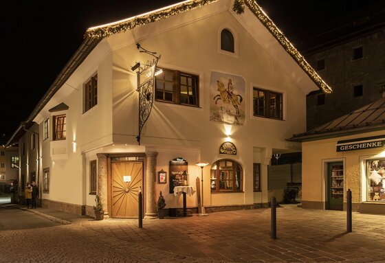 Chizzo Außenansicht bei Nacht Beleuchtetes weißes Gebäude bei Nacht mit Wandmalerei eines Reiters und weihnachtlicher Lichterkette am Dachrand.