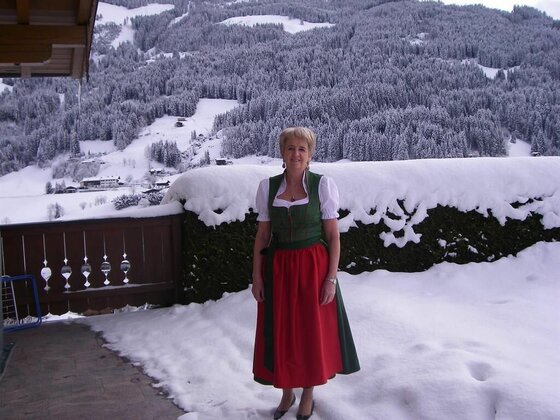 Frau in Tracht vor verschneiter Bergkulisse.