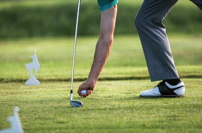 Ein Golfer bereitet sich darauf vor, den Ball zu schlagen. Im Hintergrund sind Golfmarkierungen auf dem Platz sichtbar.