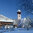 Verschneite Winterlandschaft in Aurach mit Kirche und traditionellen Holzhäusern unter blauem Himmel.