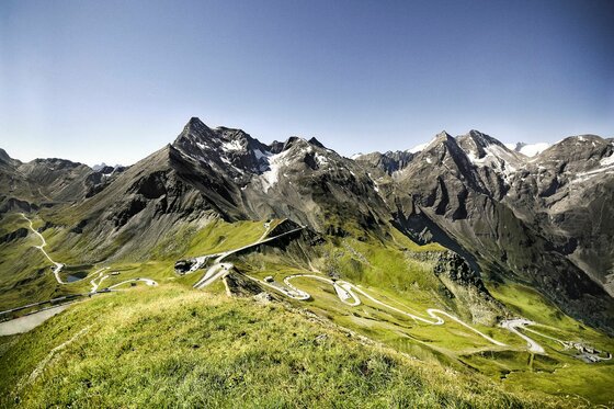 Blick von der Edelweißspitze auf die kurvenreiche Großglockner Hochalpenstraße und schneebedeckte Berggipfel.