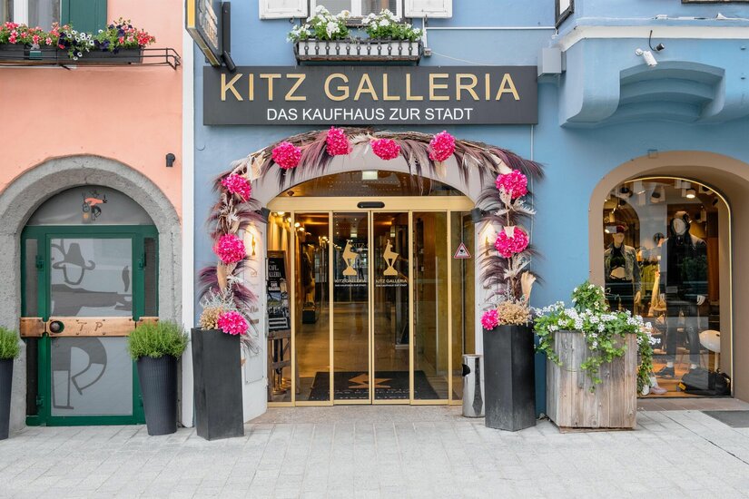 Eingang Kitz Galleria Eingangsbereich der Kitz Galleria mit goldener Glasschiebetür und Blumendekoration.