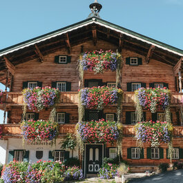 Ein traditionelles Holzhaus mit üppigen Blumenkästen, die in leuchtenden Farben blühen, vor einem klaren blauen Himmel.