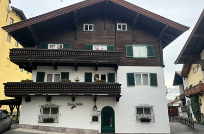 Mehrstöckiges Alpenhaus mit weißer Fassade, dunklem Holzgiebel und zwei Holzbalkonen.