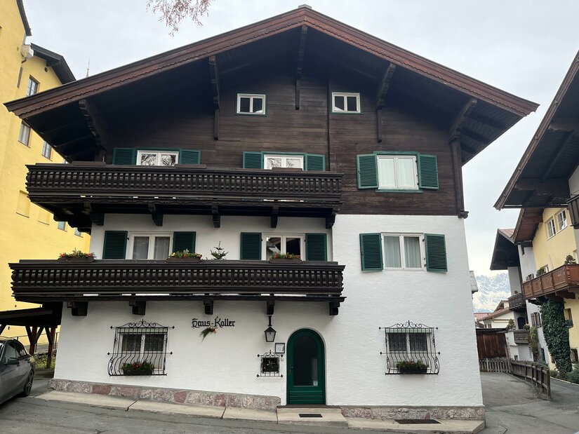 Pension Haus Koller Mehrstöckiges Alpenhaus mit weißer Fassade, dunklem Holzgiebel und zwei Holzbalkonen.