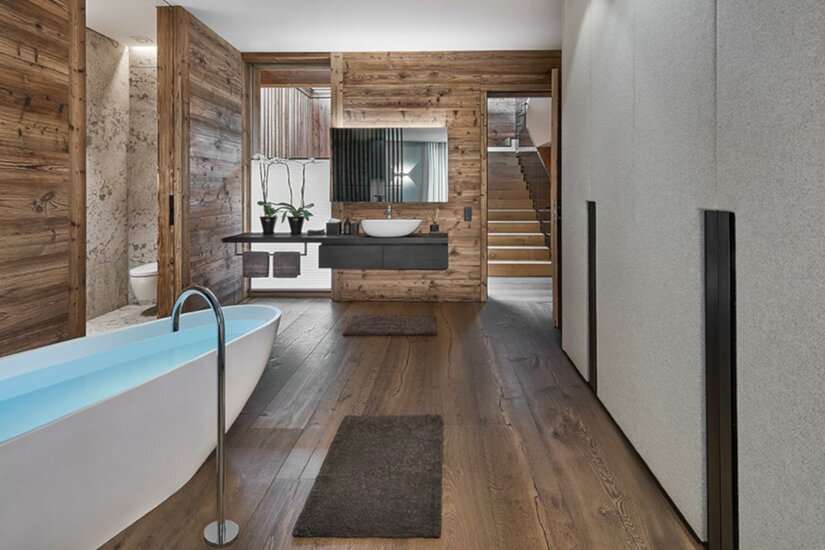 Ein modernes Badezimmer mit einer freistehenden Badewanne und Holzverkleidung. Der Raum hat große Fenster und warmen Holzboden.