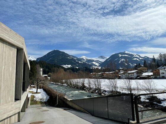 Blick auf einen Flusslauf neben einem modernen Gebäude mit schneebedeckten Bergen im Hintergrund.