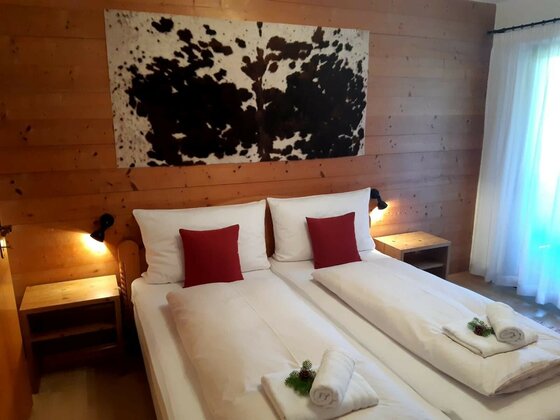 Schlafzimmer im Haus Reason Doppelbett in einem holzgetäfelten Zimmer mit Kuhfell-Wandbild und roten Kissen.
