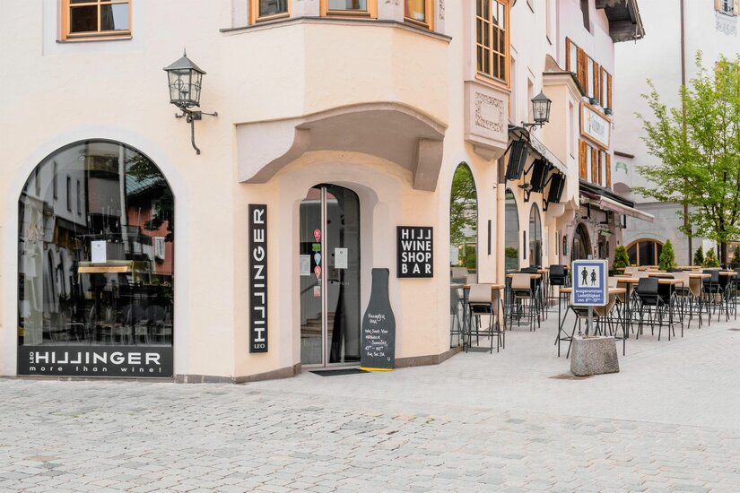 Leo Hillinger Weinshop und Bar Außenansicht einer Weinbar mit Tischen und Stühlen in einer gepflasterten Fußgängerzone.