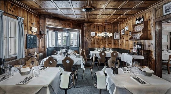 Rustikale Gaststube mit holzgetäfelten Wänden, eingedeckten Tischen und traditionellen Holzstühlen.