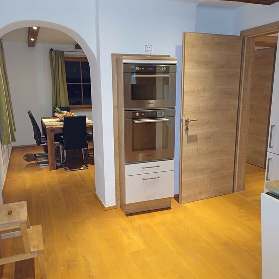 Moderne Küche mit Einbaubackofen, Holztür und Blick in den angrenzenden Essbereich mit Holztisch.