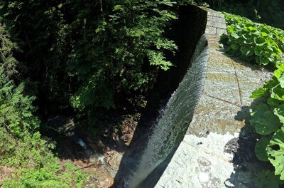Blick von oben auf eine gemauerte Steinbrücke über einen Bachlauf im Wald.