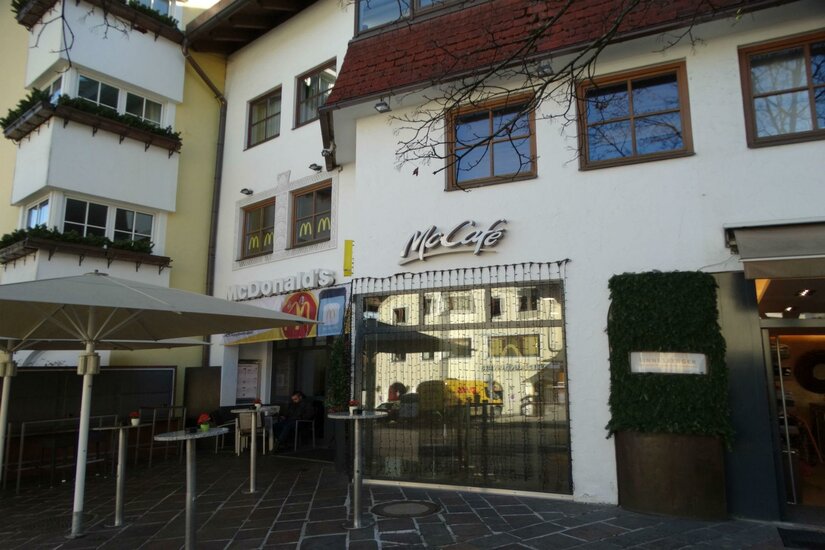 McDonalds Ein McCafé an einem Gebäudefront mit großen Fenstern. Draußen stehen ein paar Tische und Sonnenschirme.