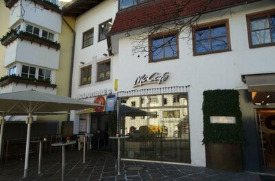 McDonalds Ein McCafé an einem Gebäudefront mit großen Fenstern. Draußen stehen ein paar Tische und Sonnenschirme.