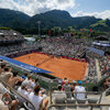 Ein lebhaftes ATP-Tennis-Match in Kitzbühel auf einem Sandplatz, umgeben von vielen Zuschauern und der Berglandschaft im Hintergrund.