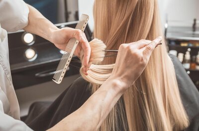 Haarschnitt im Salon Nahaufnahme einer Person, die langes blondes Haar mit Kamm und Schere schneidet.
